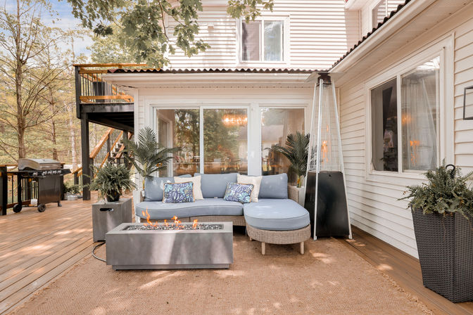 Inviting backyard wood-deck patio with blue-cushioned wicker sectional, rectangular fire pit, tall patio heater, potted plants and grill outside sliding glass doors.