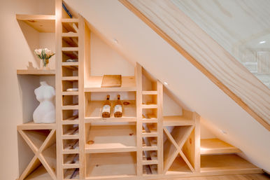 Custom light-wood built-in shelving and wine rack under a sloped ceiling, featuring two wine bottles, a decorative bust, and a vase of tulips