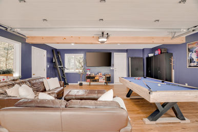 Bright home game room with blue walls and wood floors, leather sectional, blue-felt pool table, wall-mounted TV and storage cabinets — ready for game night