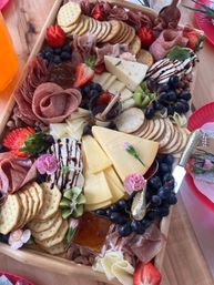 Vibrant charcuterie board on a wooden tray with sliced cheeses, assorted crackers, folded salami and prosciutto, grapes, strawberries, kiwi, honey jam and balsamic‑drizzled fresh mozzarella, decorated with edible flowers — festive grazing platter.