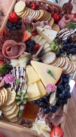 Vibrant charcuterie board on a wooden tray with sliced cheeses, assorted crackers, folded salami and prosciutto, grapes, strawberries, kiwi, honey jam and balsamic‑drizzled fresh mozzarella, decorated with edible flowers — festive grazing platter.