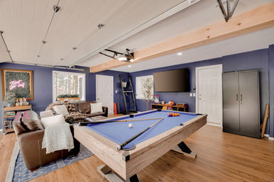Finished basement game room with blue-felt pool table, leather sofas, wall-mounted TV, navy blue walls, hardwood floors and a neon sign reading Treat Yo Self.