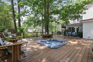 Cozy large wooden backyard deck in a leafy suburban setting with a recessed hot tub, cushioned lounge seating, swinging wooden chairs and a round bench wrapped around mature shade trees.