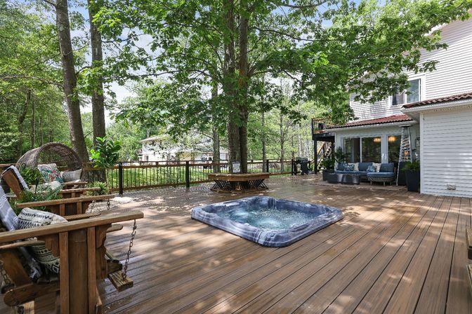 Cozy large wooden backyard deck in a leafy suburban setting with a recessed hot tub, cushioned lounge seating, swinging wooden chairs and a round bench wrapped around mature shade trees.