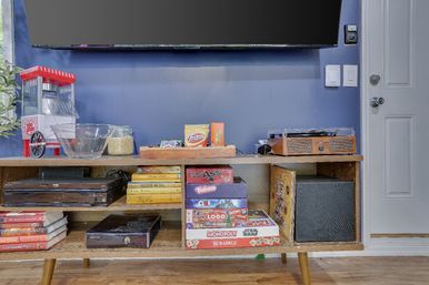 Living room entertainment console under a wall-mounted TV with a red popcorn maker, glass bowls and snack jars, a turntable, media players, books and stacked board games.