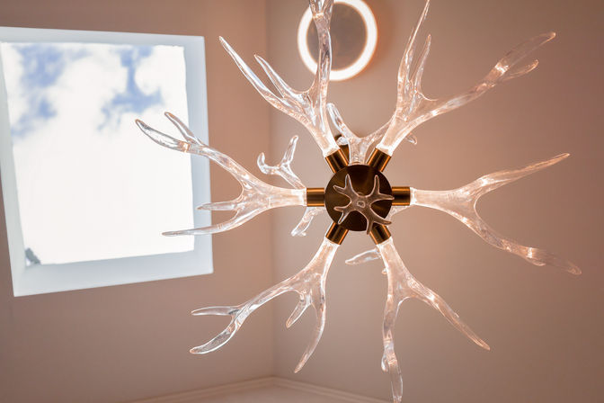 Interior ceiling light — modern glass chandelier with branching, antler-like arms glowing warm, suspended near a square skylight revealing blue sky
