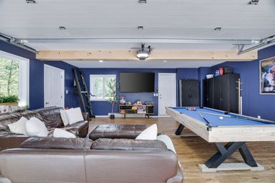 Finished garage rec room with blue walls, leather sectional, wall-mounted TV, blue-felt pool table, wood floors and black storage cabinets