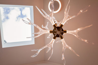 Interior ceiling light — modern glass chandelier with branching, antler-like arms glowing warm, suspended near a square skylight revealing blue sky