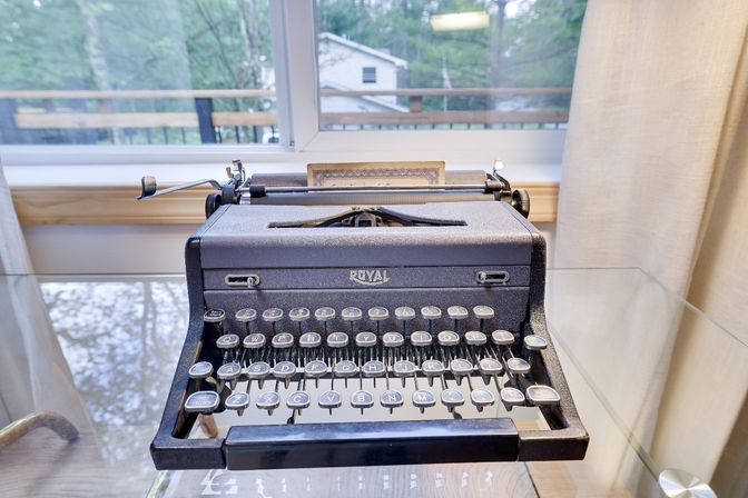 Vintage Royal typewriter on a glass desk by a sunlit window overlooking a leafy suburban backyard