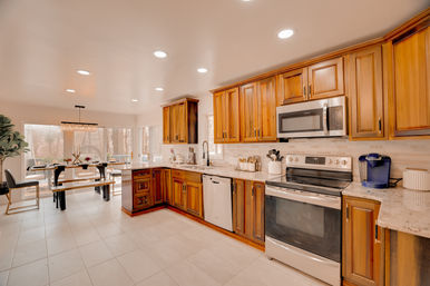 Sunny, cozy open-concept kitchen with warm wood cabinets, stainless steel oven and microwave, marble countertops, recessed lighting and a dining nook with bench seating and large windows overlooking trees.
