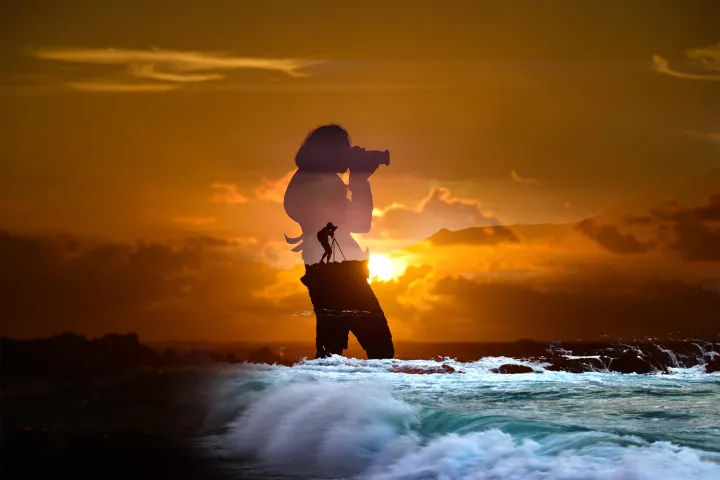 Double-exposure silhouette of a photographer on a coastal rock at golden sunset, sun low over the ocean with crashing waves in the foreground.