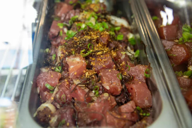 Close-up of Hawaiian-style ahi tuna poke in a stainless-steel serving tray, diced raw tuna tossed with scallions, seaweed, sesame and chili seasoning.
