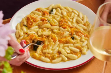 Italian gnocchi in creamy pumpkin-sage sauce with grated cheese, fork poised and a glass of white wine.