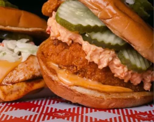 Close-up of a crispy fried chicken sandwich on a toasted brioche bun with melted cheese, zesty spicy slaw and crinkle-cut pickle slices.