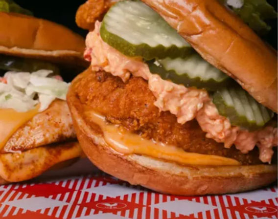Close-up of a crispy fried chicken sandwich on a toasted brioche bun with melted cheese, zesty spicy slaw and crinkle-cut pickle slices.