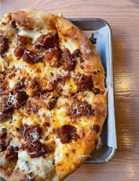 Close-up of a cheesy pizza topped with browned sausage crumbles and grated Parmesan, served on a metal tray on a light wooden restaurant table.