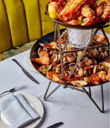 Two-tier seafood tower piled with clams, mussels and shrimp, garnished with herbs and lemon, served on a white-tablecloth at a coastal-style restaurant