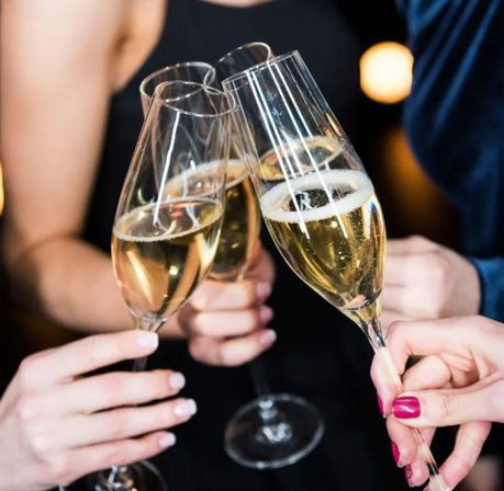 Three hands clinking champagne flutes filled with bubbly for a celebratory toast at a party or night out