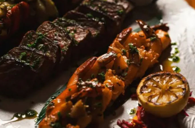 Surf-and-turf plate with a grilled shrimp skewer, seared steak slices, charred lemon half and herb drizzle — restaurant-style entree
