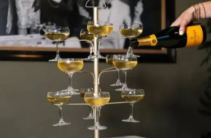 Tiered champagne tower of coupe glasses on a metal stand being filled from a sparkling wine bottle, golden bubbly for a festive celebration
