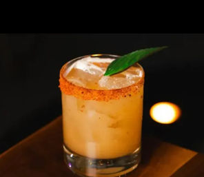 Zesty orange cocktail in a lowball glass with ice, chili-spiced rim and a green leaf garnish on a dim bar background