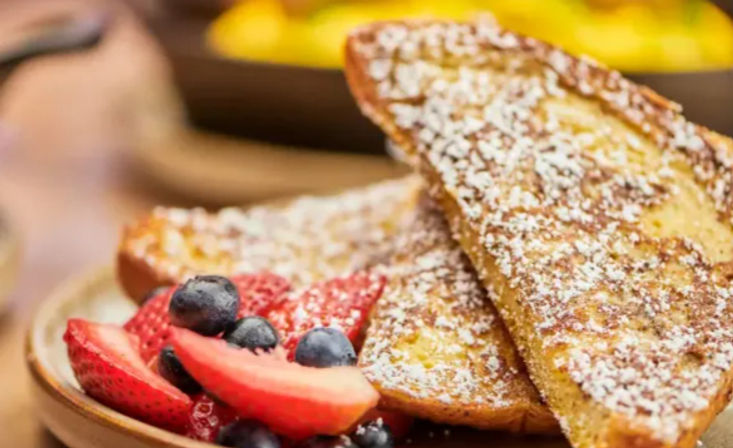 Close-up of golden French toast dusted with powdered sugar, served with sliced strawberries and blueberries on a breakfast/brunch plate