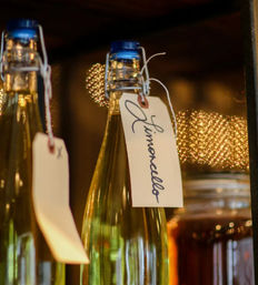 Swing-top glass bottles labeled 'Limoncello' with handwritten tags on a shelf, warm golden bokeh lights in the background.