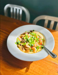 Southern-style shrimp and grits: creamy grits topped with shrimp, sautéed mushrooms and chopped green onions in a white bowl with a spoon on a wooden table in a casual restaurant setting