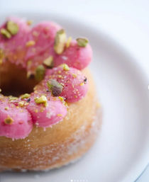 Close-up of a glazed donut with pink frosting dollops and crushed pistachios on a white plate