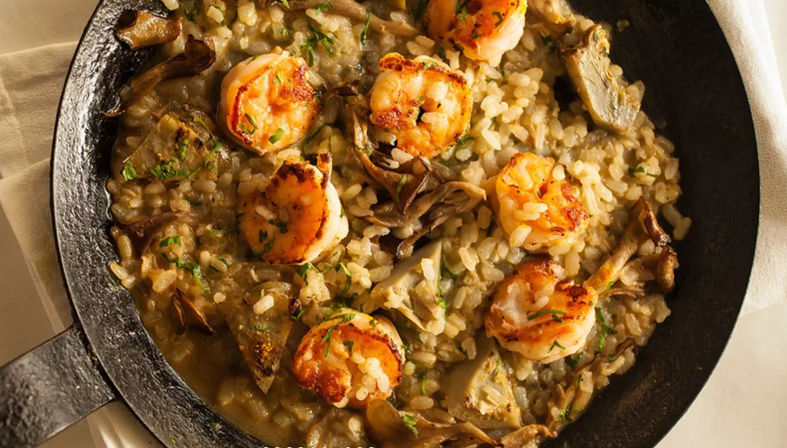 Cast-iron skillet of creamy mushroom risotto topped with golden seared shrimp and chopped parsley