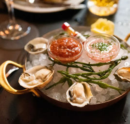 Fresh raw oysters on crushed ice in a gold-handled pan, garnished with sea beans and lemon, served with cocktail and mignonette sauces — restaurant seafood platter