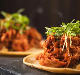 Close-up of mouthwatering Mexican pulled-pork tacos on corn tortillas topped with spicy sauce and fresh microgreens, shallow focus with blurred background