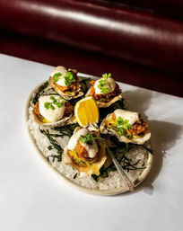 Gourmet oysters on the half shell topped with crispy crumbs and creamy sauce, garnished with fresh herbs, served on coarse salt and seaweed with a lemon wedge — seafood appetizer