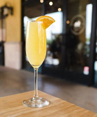 Bright mimosa in a champagne flute garnished with an orange wedge, set on a wooden table at a cozy brunch cafe