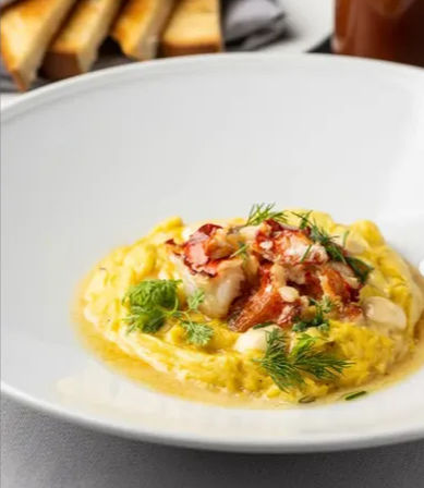 Creamy saffron risotto crowned with chopped lobster meat and fresh dill on a white plate, with toasted bread blurred in the background