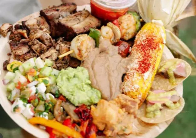 Mexican-style street-food plate with grilled elote dusted in chili and cheese, shrimp-and-vegetable skewer, chopped grilled chicken, two mini tacos topped with guacamole and pickled onions, refried beans, fresh guacamole, pico de gallo and sautéed peppers.