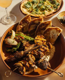 Mediterranean-style mixed grill platter with lamb chops and skewers, charred lemon, pita wedges, roasted peppers and onions, and creamy dip