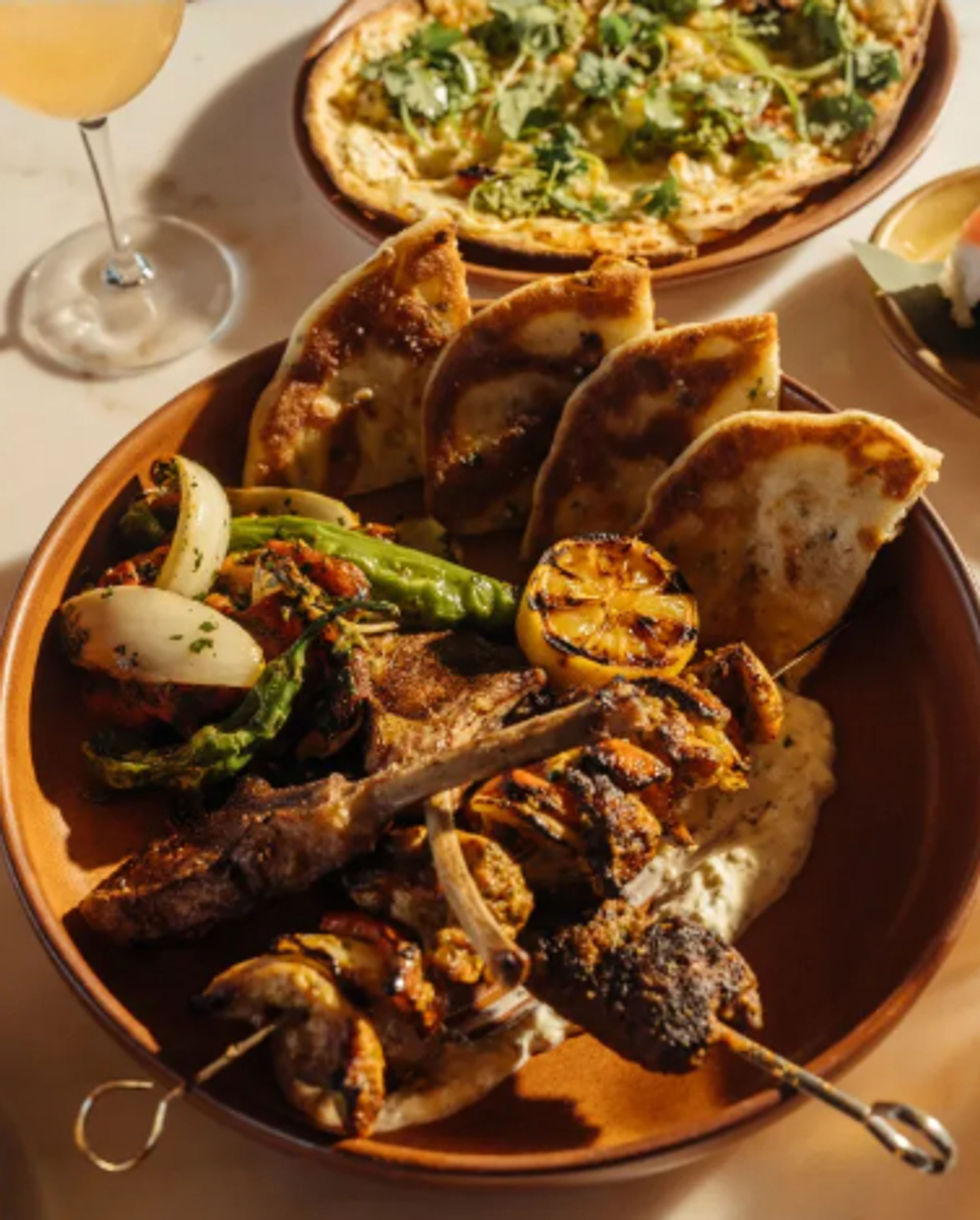 Mediterranean-style mixed grill platter with lamb chops and skewers, charred lemon, pita wedges, roasted peppers and onions, and creamy dip