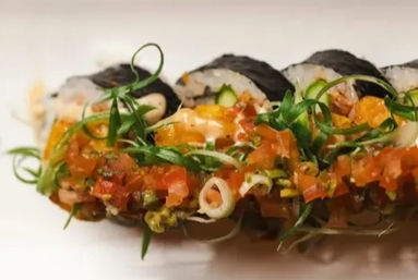 Close-up of nori-wrapped sushi roll topped with diced tomato salsa, curled scallions and a zesty spicy mayo drizzle