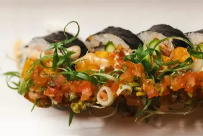 Close-up of nori-wrapped sushi roll topped with diced tomato salsa, curled scallions and a zesty spicy mayo drizzle