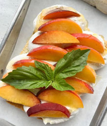 Close-up of ricotta toast topped with sliced ripe peaches, honey drizzle and fresh basil on a parchment-lined baking sheet.