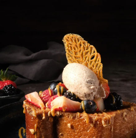 Decadent gourmet dessert: thick toasted brioche topped with strawberries, raspberries, blueberries and blackberries, a scoop of speckled vanilla ice cream, caramel drizzle and a delicate lace tuile garnish