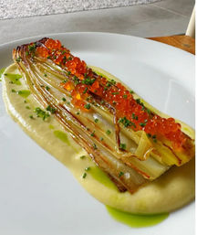 Grilled leek topped with bright salmon roe and chopped chives, served on a smooth potato purée with herb oil — plated as a modern fine-dining appetizer.