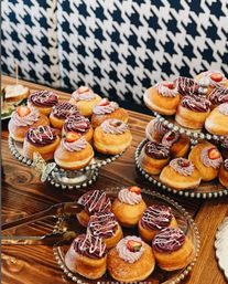 Mini filled donuts topped with purple and pink whipped frosting and fresh strawberry slices, arranged on tiered silver platters on a wooden table with a houndstooth backdrop