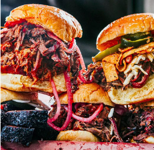 Close-up of mouthwatering smoked BBQ pulled beef sandwiches on brioche buns, topped with pickled red onions, jalapeños, shredded cheese and crunchy tortilla strips — hearty barbecue platter.
