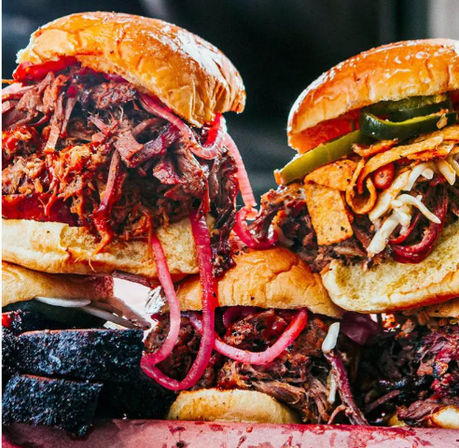 Close-up of mouthwatering smoked BBQ pulled beef sandwiches on brioche buns, topped with pickled red onions, jalapeños, shredded cheese and crunchy tortilla strips — hearty barbecue platter.