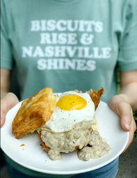 Plate with flaky biscuit topped with creamy sausage gravy and a sunny-side-up egg — Nashville-style breakfast sandwich