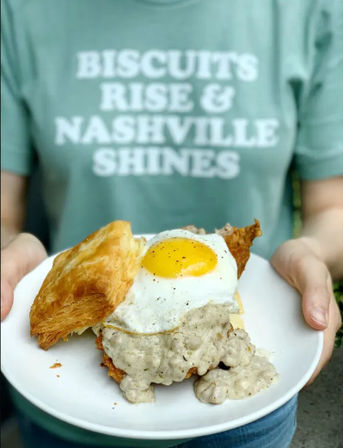 Plate with flaky biscuit topped with creamy sausage gravy and a sunny-side-up egg — Nashville-style breakfast sandwich