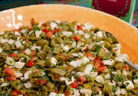Colorful Mexican nopal (cactus) salad with diced nopales, tomatoes, white cheese, onion and cilantro in an orange serving bowl
