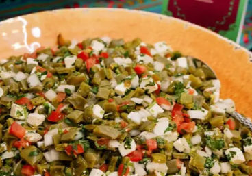 Colorful Mexican nopal (cactus) salad with diced nopales, tomatoes, white cheese, onion and cilantro in an orange serving bowl